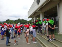 黄緑色のバンダナを肩に巻いた生徒を先頭に赤白帽を被った生徒が縦に整列している写真