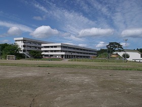 白壁の3階と4階建ての校舎が、青空の下で静かに建っている現代の学校を校庭から撮影した写真