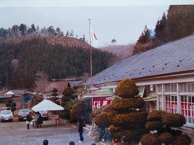 窓に紅白の幕が飾られた校舎の前に白いテントが設置され、国旗が掲げられた写真