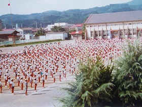 広い校庭で赤白帽をかぶった大勢の子どもたちが整列している写真