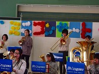 ミニコンサートの飾りつけの前でトランペット、トロンボーンを演奏している生徒を写した写真