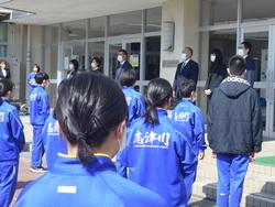 校舎前に横一列に並んで立った先生たちと向かい合って、青いジャージを着た生徒たちが整列ている写真
