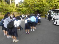 生徒たちが駐車場に停まったバスの前に並び、礼をしている様子の写真