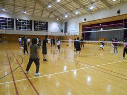 体育館の明るい照明の下で、複数の人たちが二つのチームに分かれてバレーボールをしている様子を写した写真