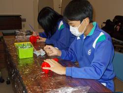 青いジャージを着た男女の児童が、赤い張り子の牛に絵を描いている様子の写真