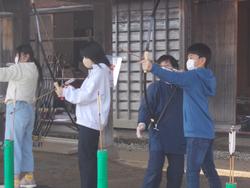 屋外で弓道の体験をしている児童たちが、指導者に教わりながら弓を構えている様子の写真