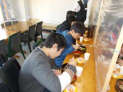 数人の児童たちがアクリル板越しに向かい合い、黙々と食事をしている様子の写真