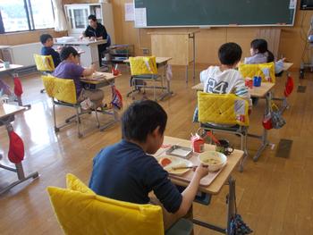 小学校の教室で、児童たちがそれぞれの机で前を向いて給食を食べている様子の写真
