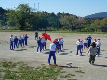 赤い旗を持った男の子が1人前に立ち、その後ろに5列に並んでいる赤組の児童たちの写真