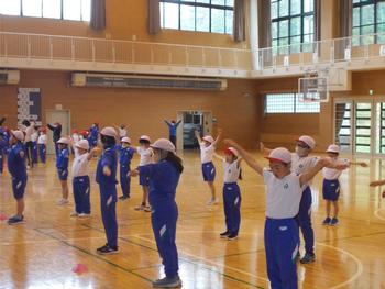 ジャージ姿の児童が両手を水平に横にあげ体育館内で運動会の並び方の練習をしている写真