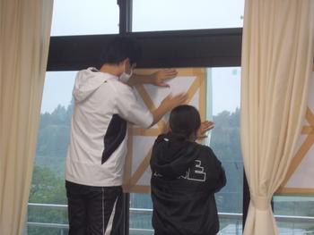 校舎の窓に大きな紙を貼っている男性と女性の後姿を写した写真