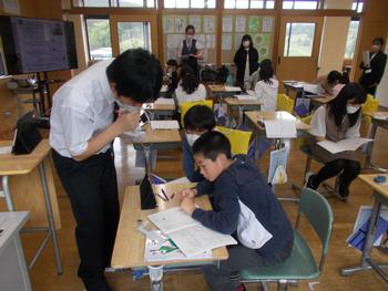 教室の席に児童たちが座り、複数の職員が生徒の近くに座ったり立って指導をし、その様子を参観している職員がいる様子の写真