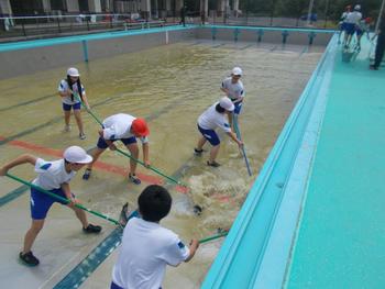水が残ったプールに入った生徒たちが、デッキブラシを使いながら底の清掃をしている写真