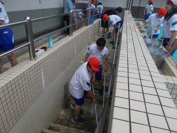 体操服姿の児童達が階段状になった通路などをブラシを使い掃除したり、手洗い場でバケツに水をくんだりしているプール掃除での写真