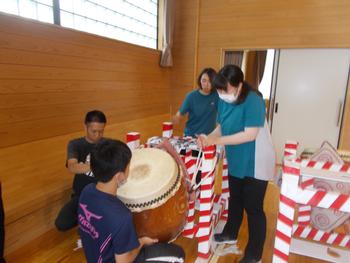女性2名と男性2名が大太鼓を台に設置している様子を写した写真
