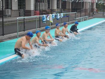 プールのふちに座り、足を水の中に入れて体に水をかけている男子児童6名の写真