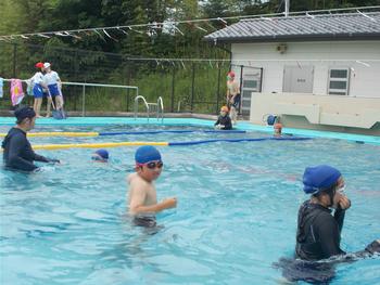 プールにはいり、冷たそうに身をすくめて歩いている児童たちの写真