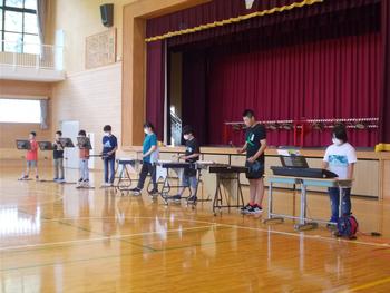 舞台の前に8名の児童が並んでリコーダーや木琴,鉄琴,キーボードなどを演奏している写真