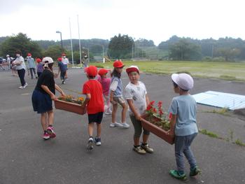 赤白帽子を被った児童が2人1組でプランターを運んでいる写真