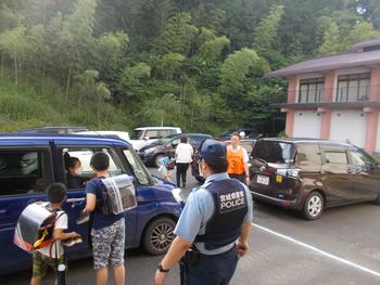 警察官の男性が見守る中、迎えに来た保護者の車に児童たちが乗っている写真