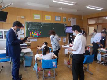教室内の児童の机の周りで先生方が授業を参観している様子を写した写真