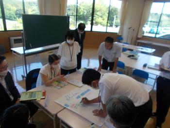 模造紙を置いた机の周りに数名の教職員が集まり、1人の男性が模造紙に記入している様子の写真