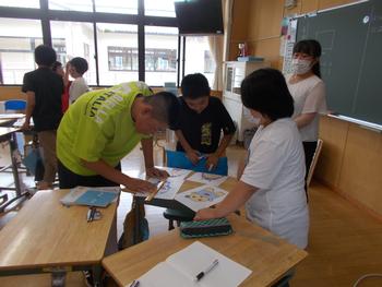 3名の班で一つの机の周りに立ちながらキャラクターの長さを物差しで測っている学習参観の写真