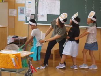 小学校の教室で1年生の子どもたちが『大きなかぶ』の音読発表を動きや表情を交えて披露している写真