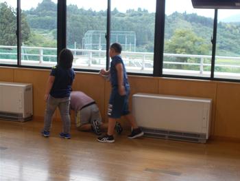 大きな窓を拭いている男の子とその前を雑巾がけしている男の子、横に立つ男の子の教室内での大掃除の写真