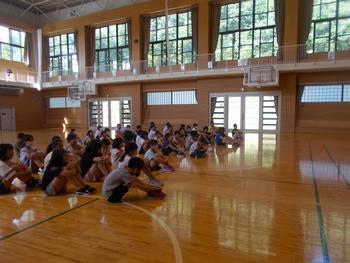 児童達が体育館の床に座っている様子を写した写真