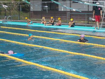 プールの中でビート板を使い泳いでる子供や上に上がってみている5名の児童達の校内水泳記録会での写真