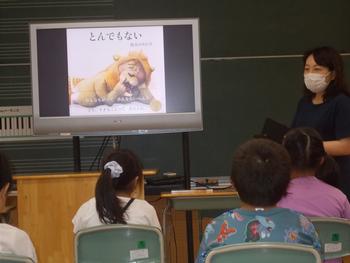 子供たちがモニターに映し出された「とんでもない」の絵本の表紙を見ている読み聞かせの写真
