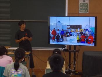 女性の隣のモニターを見ている子供たちの写真