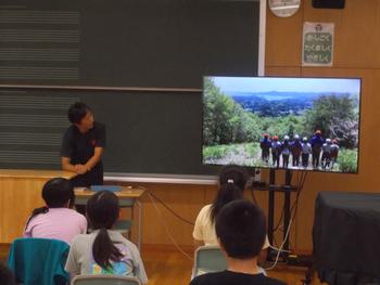 モニターを見ながら女性が説明し、子供たちが耳を傾けている出前講座の写真