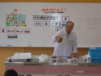 ホワイトボードに「おみそのヒミツ」と書かれ、男性が説明をしている写真