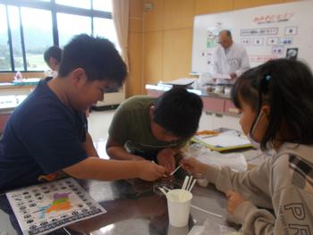 3名1組で紙コップから綿棒のようなものを取り出し実験をしている様子を写した写真