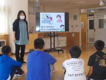 男の子4名が床に座り女性がモニターを使い説明をしている写真