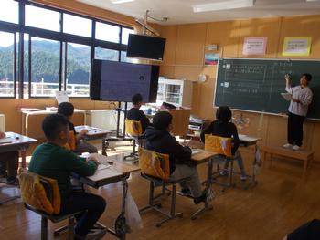 黒板に背を向け生徒たちに話している先生と授業を受けている子供たちの写真