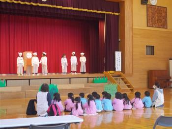 幼稚園の園児が体育館に座りながら、舞台の劇を楽しんでいる写真
