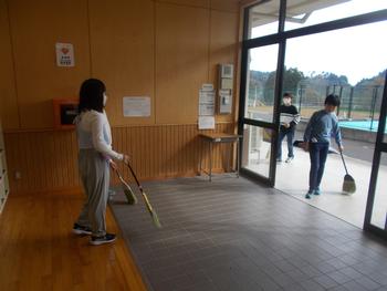 昇降口の外と入り口内をほうきで掃除している子供たちの写真