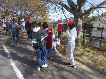 歩道の落ち葉をほうきを使い子供たちがみんなで掃除をしている写真