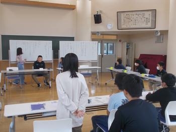 ロの字に設置された長机に各委員会の子供たちが座り、正面のホワイトボードに一人の女の子が立っている委員会時の写真