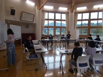 ロの字に設置された長机に各委員会の子供たちが座り、左奥の男の子が話をし正面のホワイトボードに一人の女の子が記入している委員会時の写真