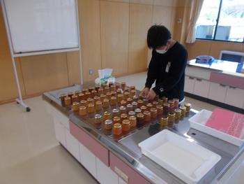 調理台に並べられた瓶のジャムに男の子がシールを貼っている写真