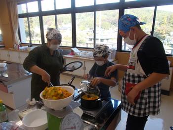 ボールにいれたジャムの原料をはかりにのせ、3名の児童がエプロン姿で鍋でジャムを煮詰めている写真