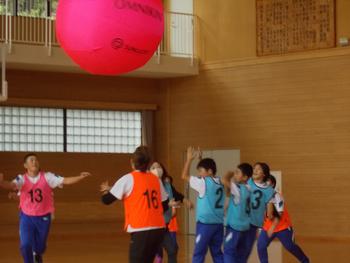 大きな赤い球体を床に落ちないようにチームに分かれて触っている体育館内の写真