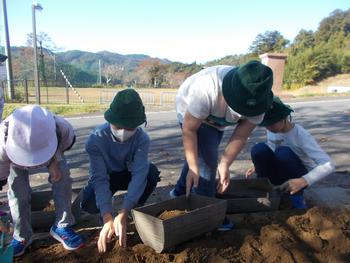 4名の人たちがしゃがみこんでプランターに土を入れている写真