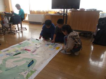 大きな模造紙の橋で生徒3人が集まりしゃがみこみながら話し合いをしている写真