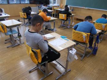 机においた回答用紙を前に考えている男の子を斜め後方から写した写真