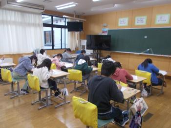 机に座った子供たちが必死にテストの回答用紙に記入している様子を教室の右斜め後ろから写した写真